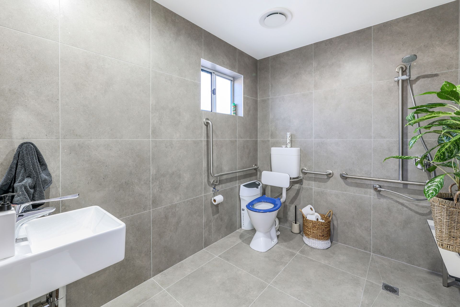 Accessible bathroom with gray tiles, toilet, sink, and grab bars.
