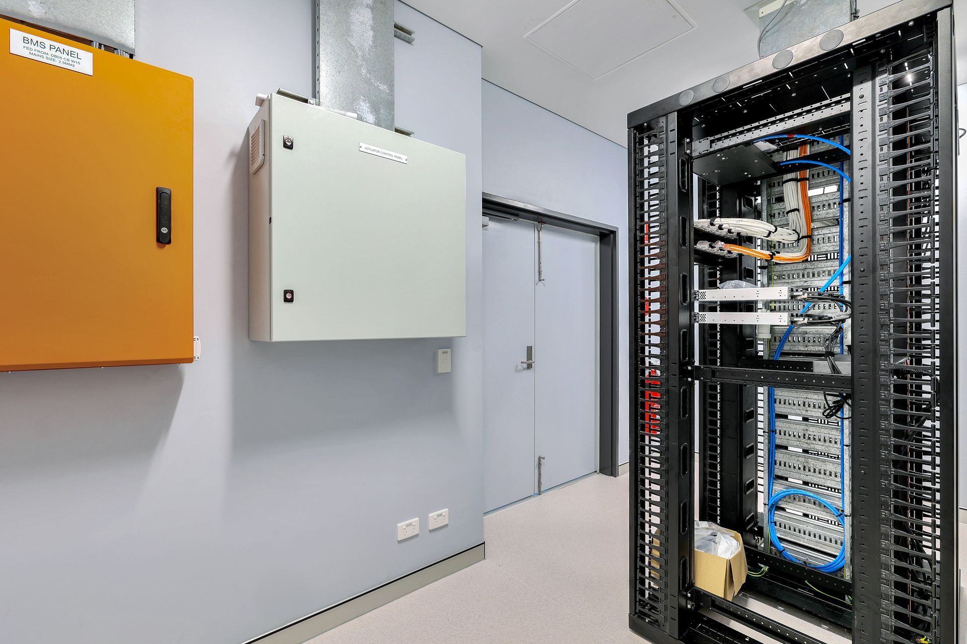 Server room with an open server rack, electrical boxes, and a doorway.