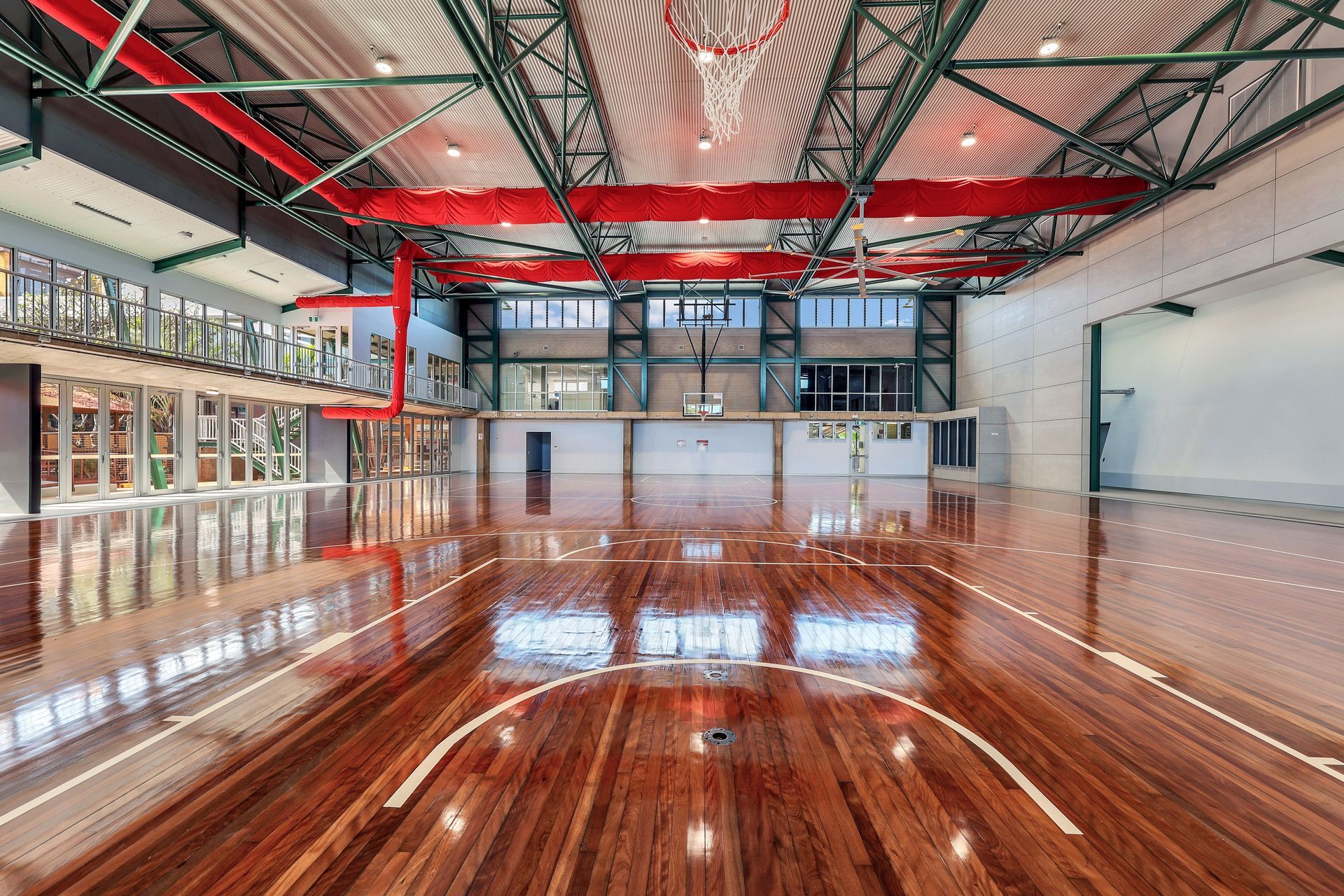 Wooden basketball court with red beams, windows, and hoops.