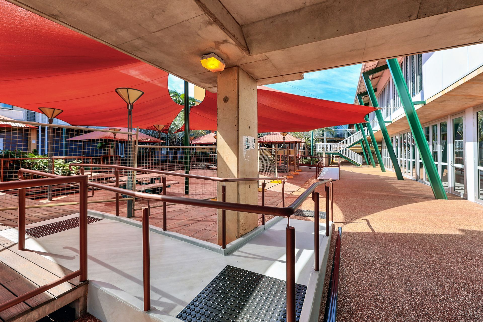 Ramp and walkway under red shade structures, exterior view of a building complex.