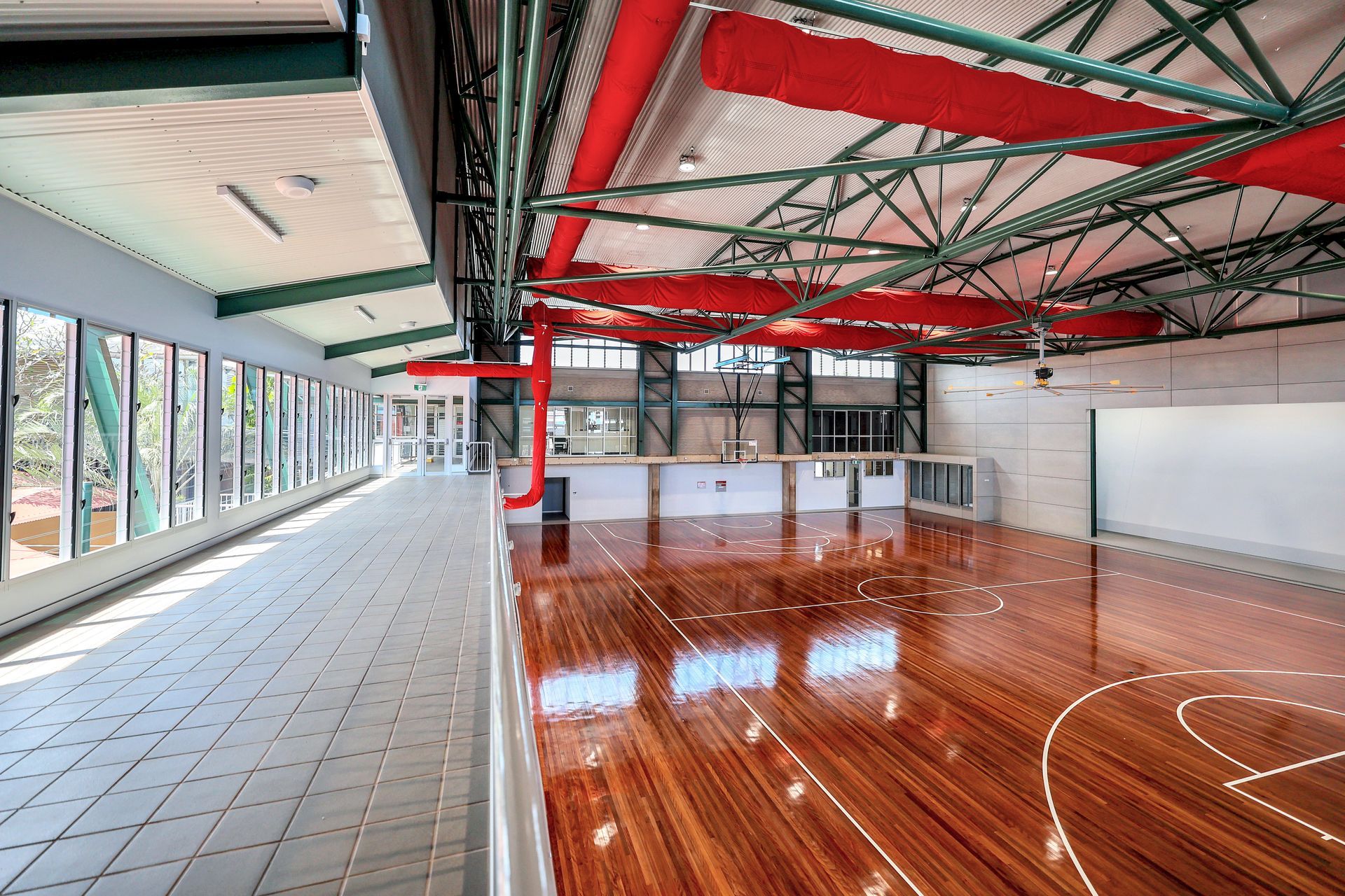 Indoor gym with hardwood floor, red pipes, and windows along the left wall.