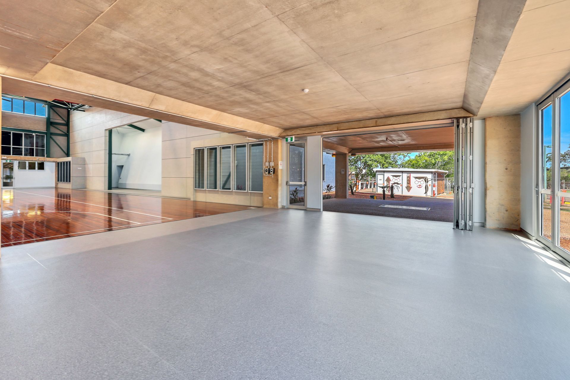 Empty, open-concept room with large windows. Concrete ceiling, polished gray floor, and an open doorway to an outdoor area.