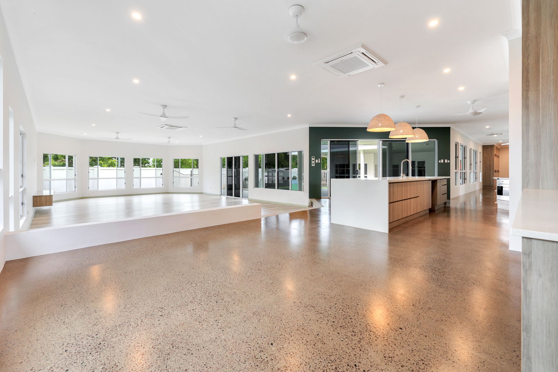 Spacious, bright room with polished concrete floors, a raised platform, and windows. Features a kitchen island with pendant lights.