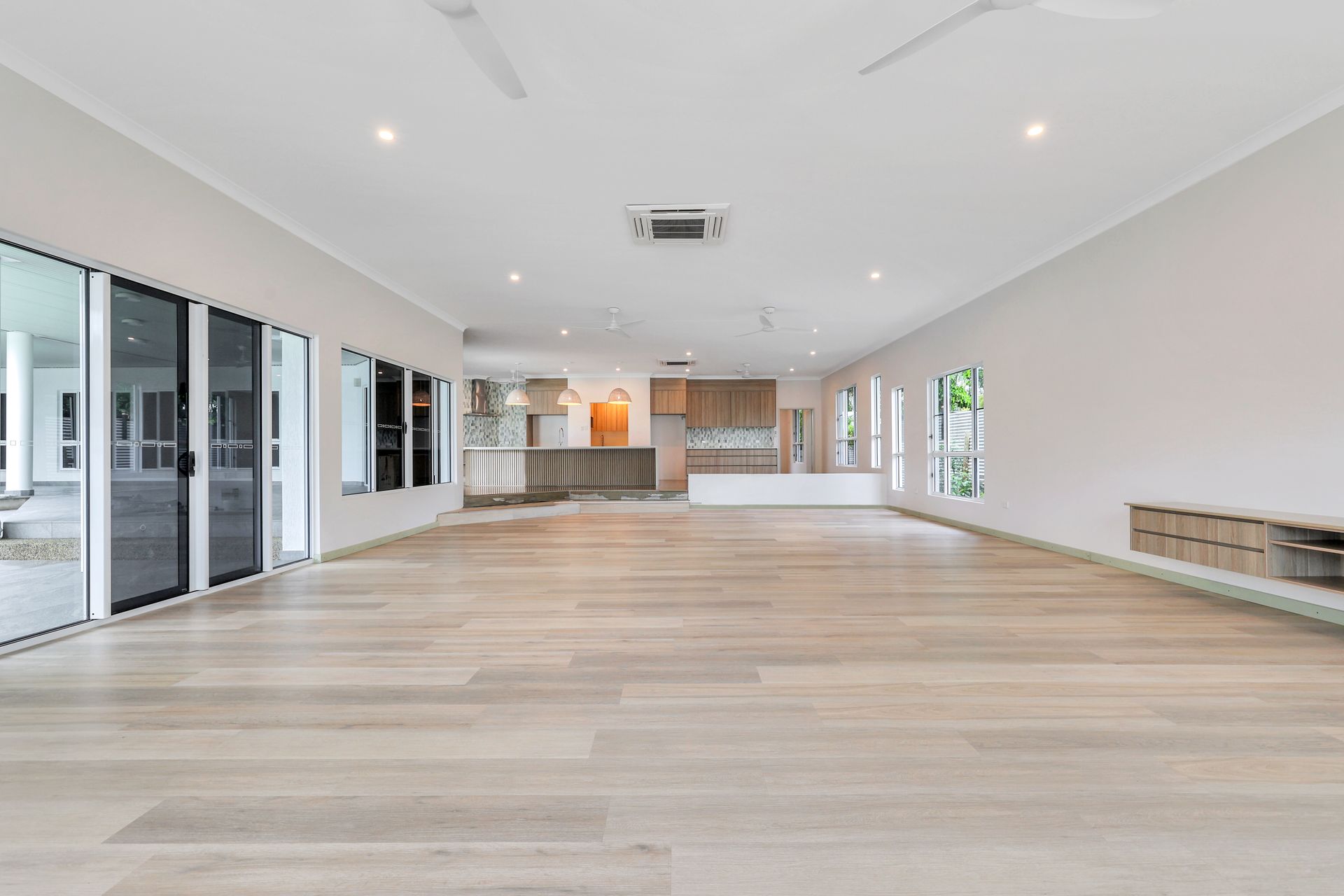 Spacious, empty room with light wood floors, sliding glass doors, and minimalist design.
