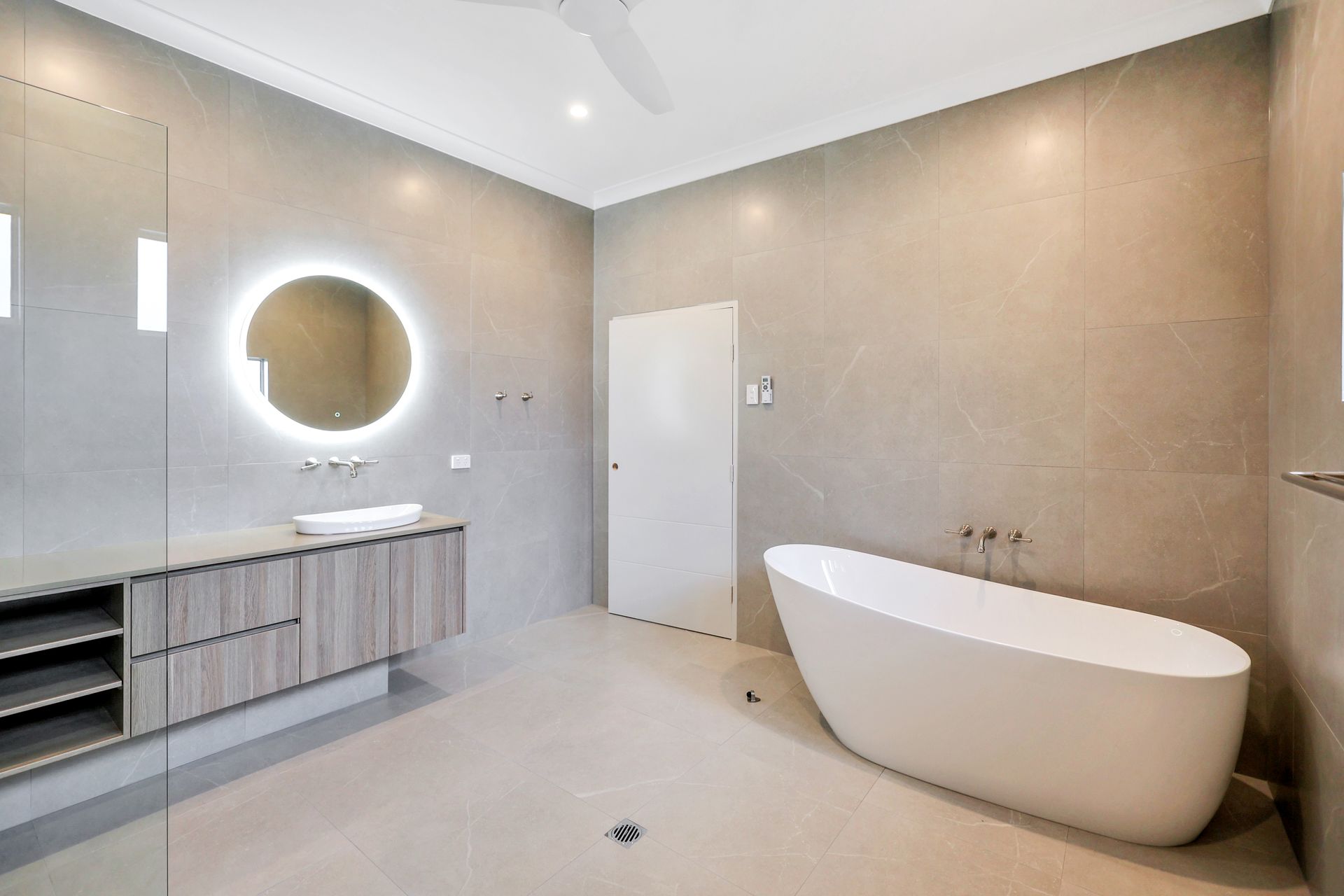 Modern bathroom with white tub, wood vanity, round mirror, and gray walls.