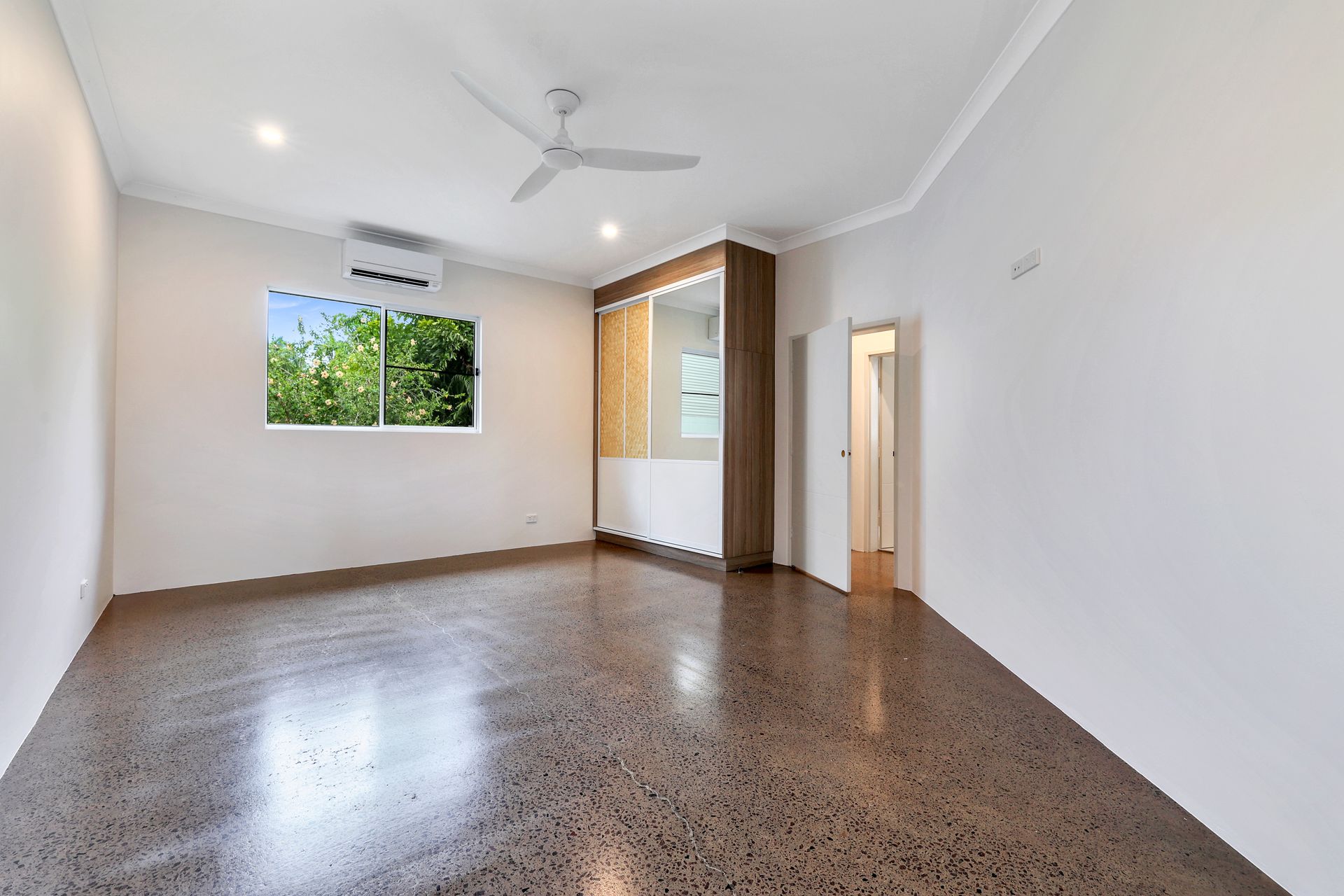 Empty room with concrete floor, white walls, and a built-in cabinet. Window shows greenery.