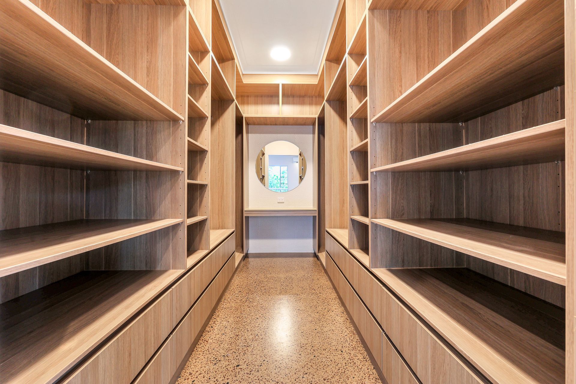 Walk-in closet with light wood shelves and drawers on both sides, a vanity, and a mirror.