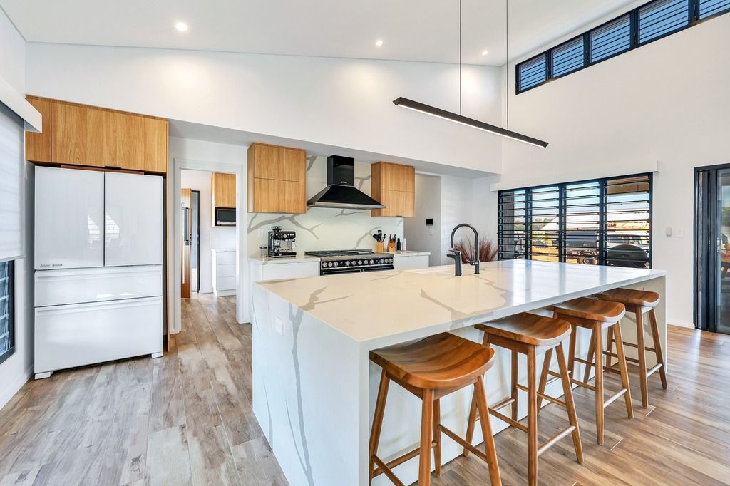 Modern kitchen with large island, wood stools, light cabinets, and tall windows.