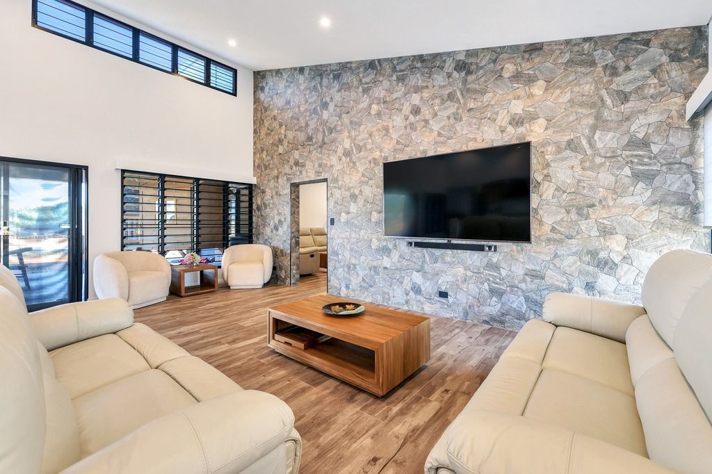 Living room with stone accent wall, TV, cream-colored couches, and wooden coffee table.