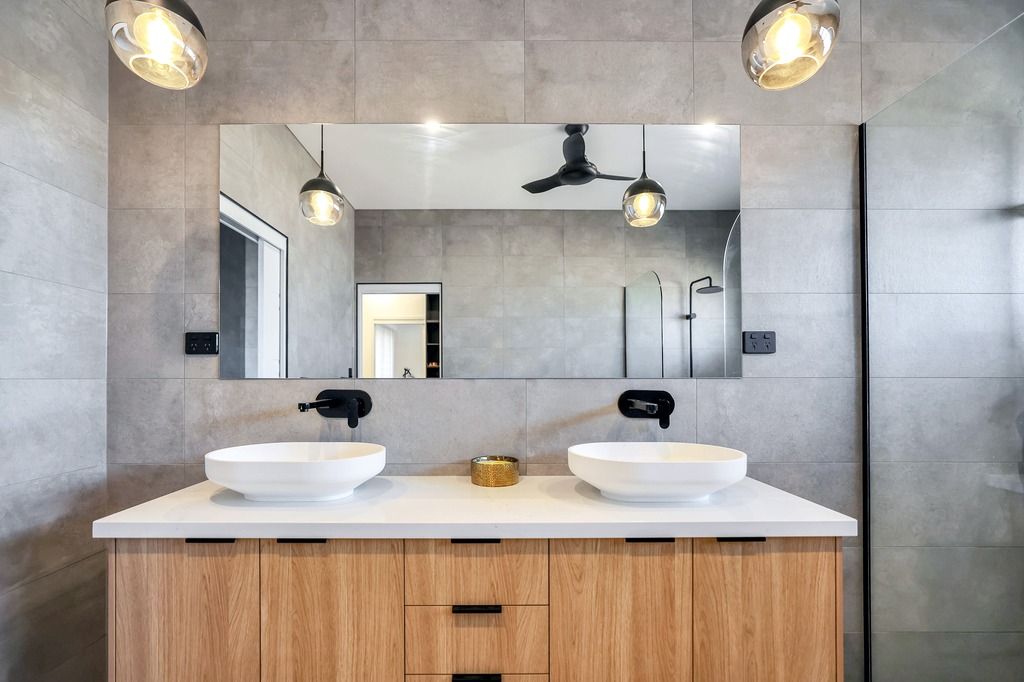 Bathroom with wood vanity, white sinks, large mirror, and gray tile.