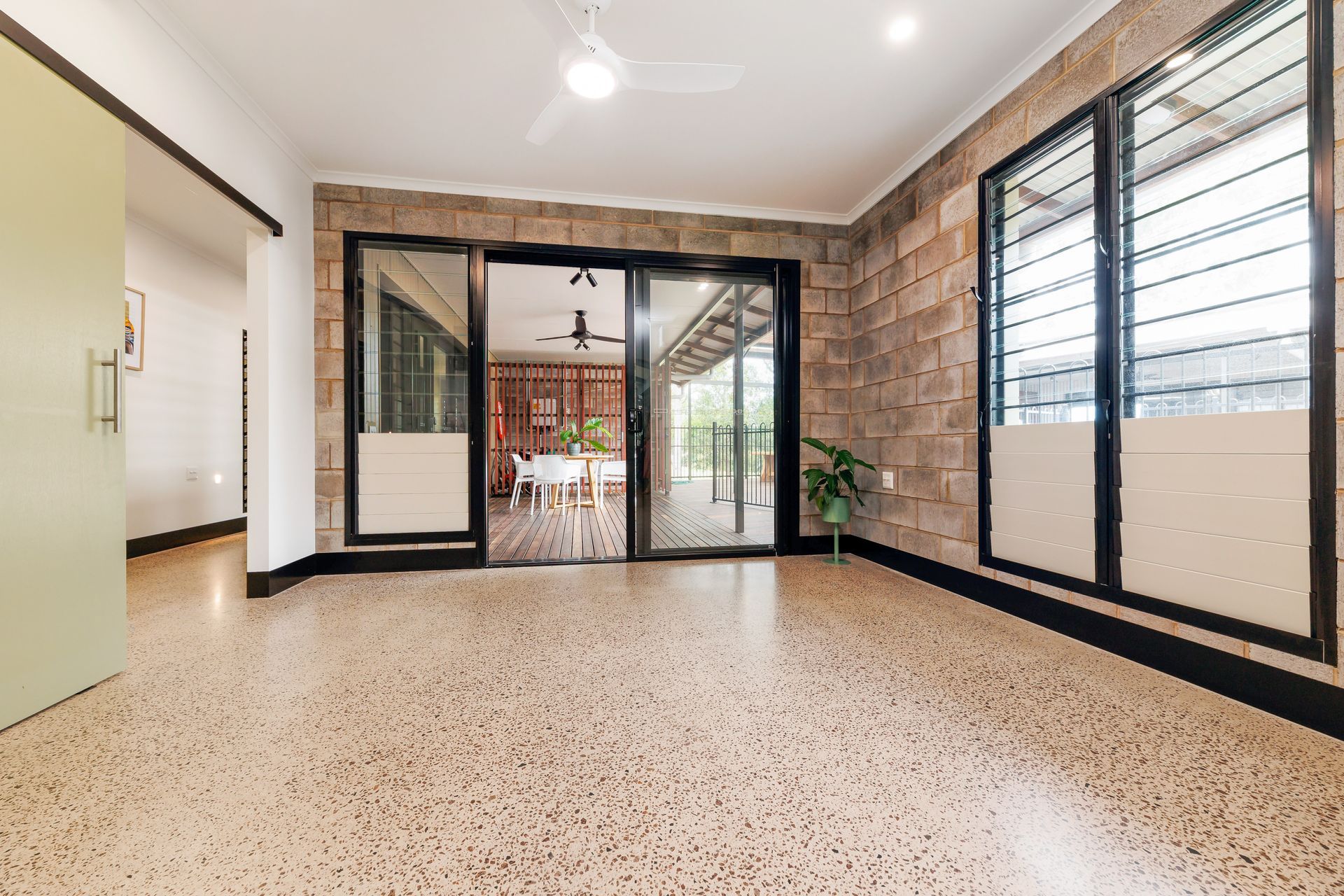 Spacious room with concrete block walls, large glass doors, and terrazzo flooring, opening to a dining area.
