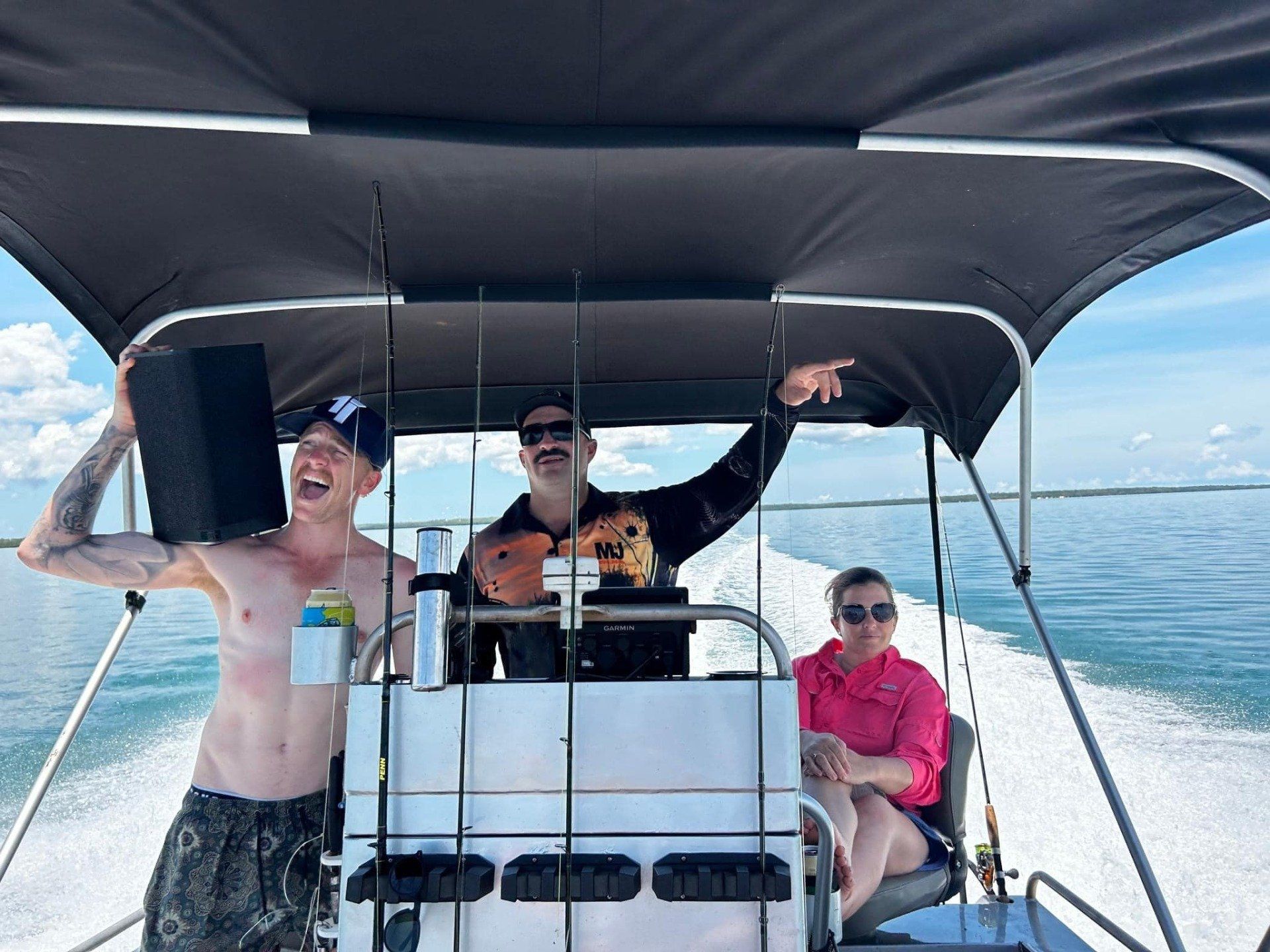 Three people on a boat, enjoying the sun. One points, another laughs, a third sits; blue water, sunny sky.