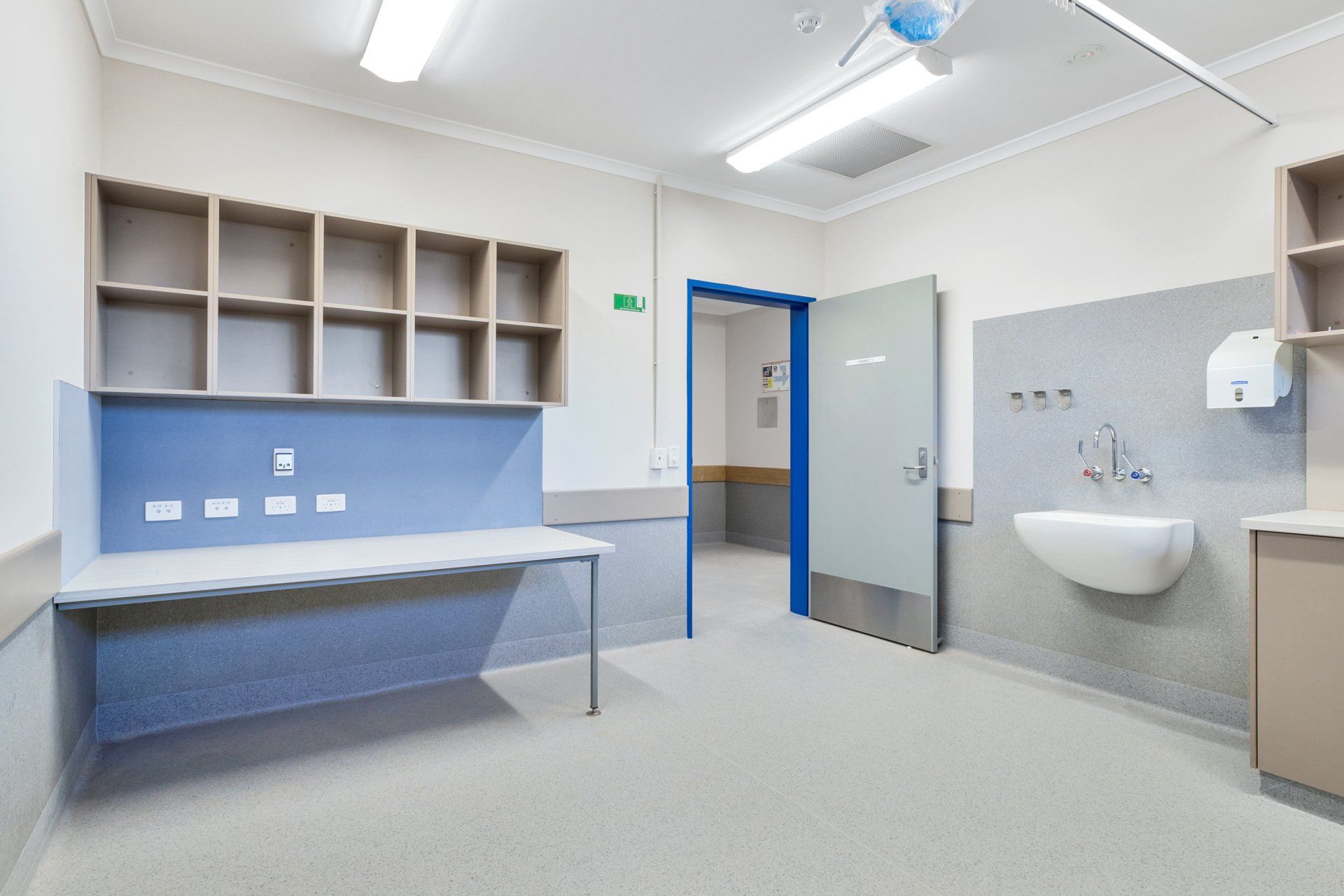 A medical room with a counter, sink, shelves, and open doorway to another room.
