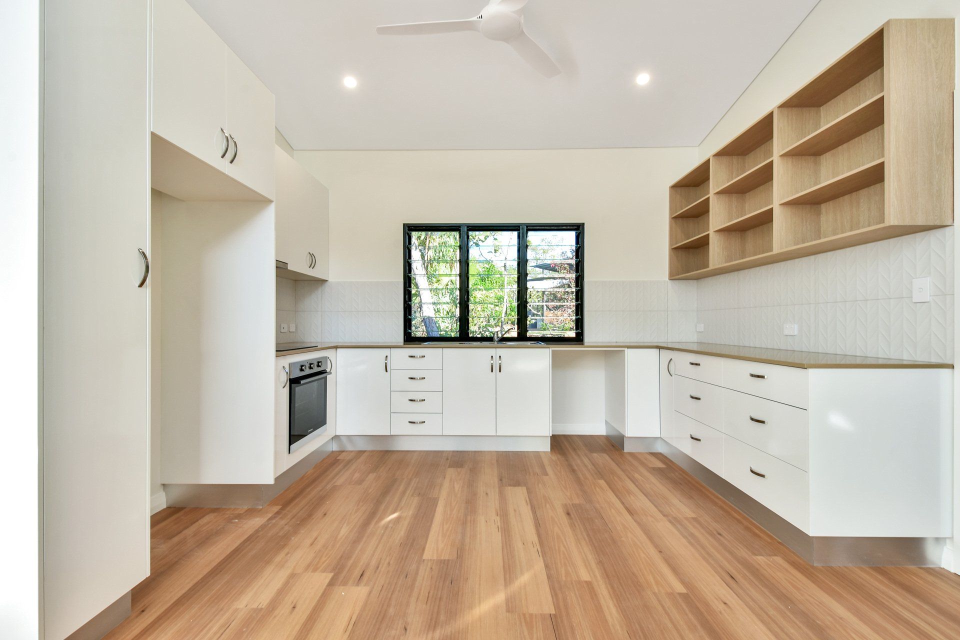 Empty kitchen with white cabinets, wooden floor, and light wood shelves.