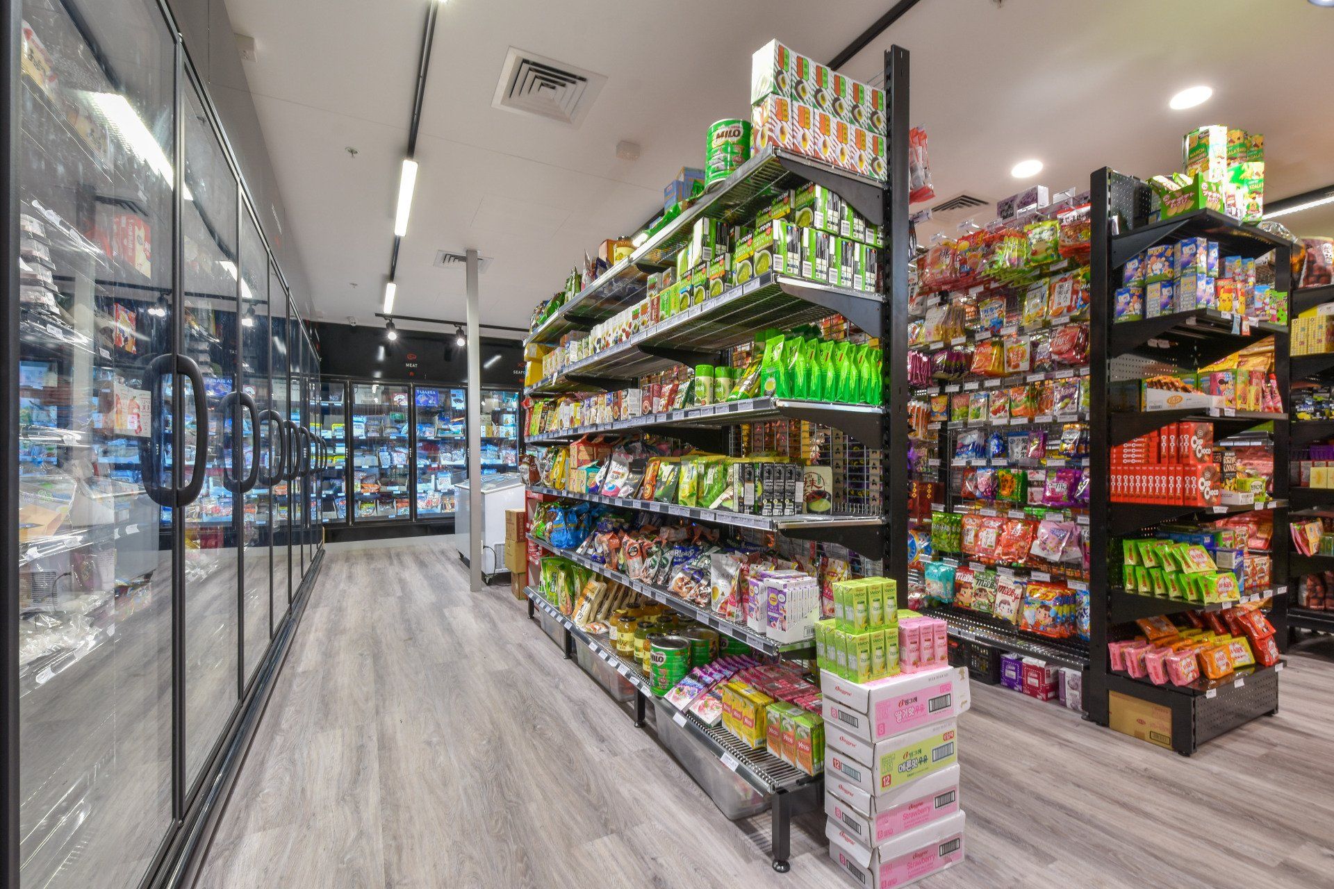 Grocery store aisle with shelves stocked with various products. Refrigerated cases on the left.
