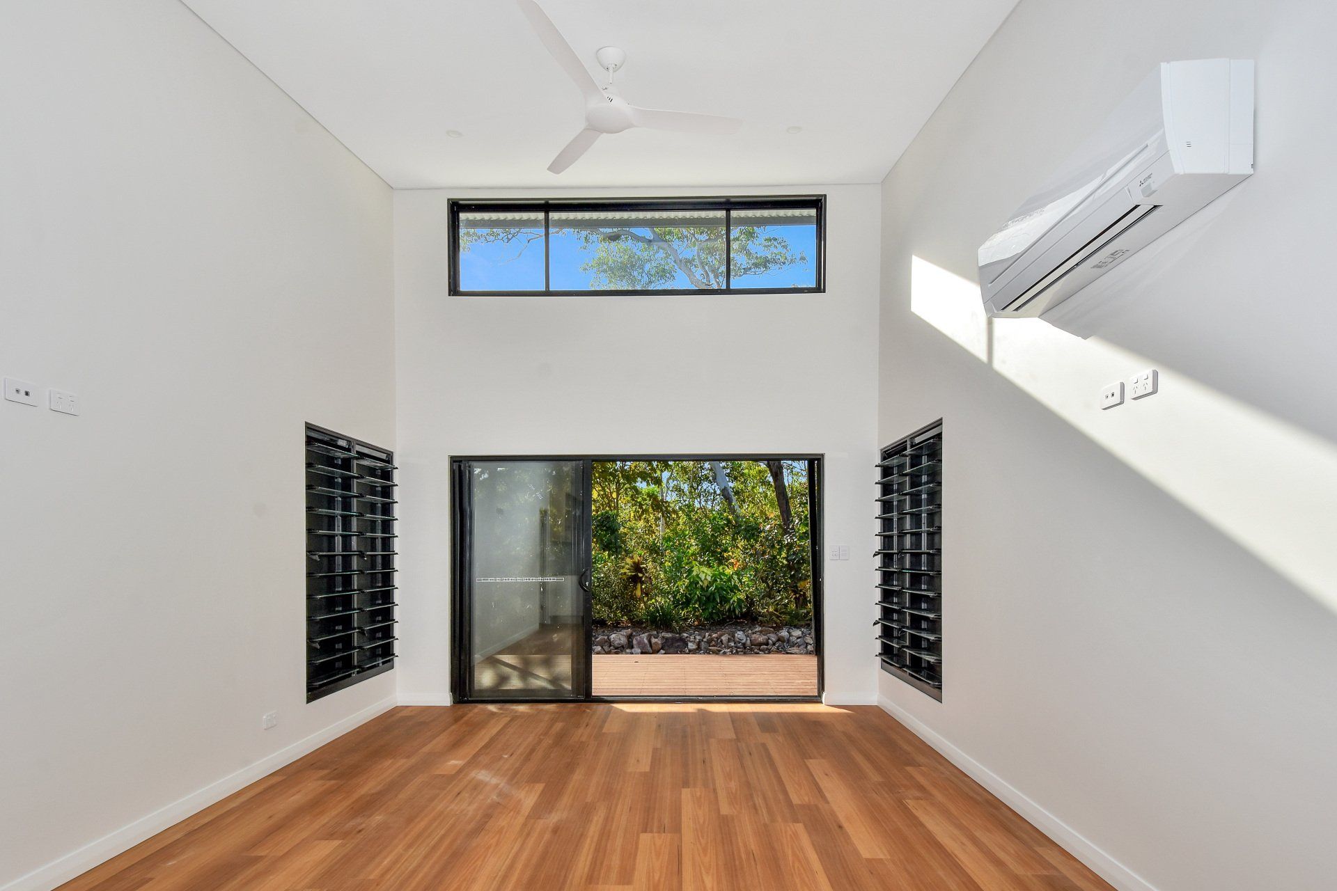 Empty room with hardwood floors, large windows, and air conditioning unit.