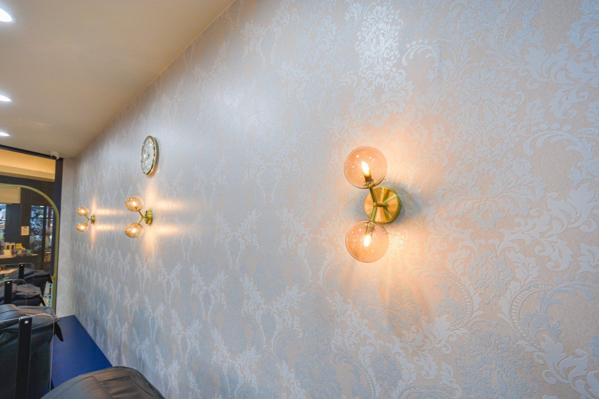 Wall with decorative silver texture, gold sconces with globes, and a clock.