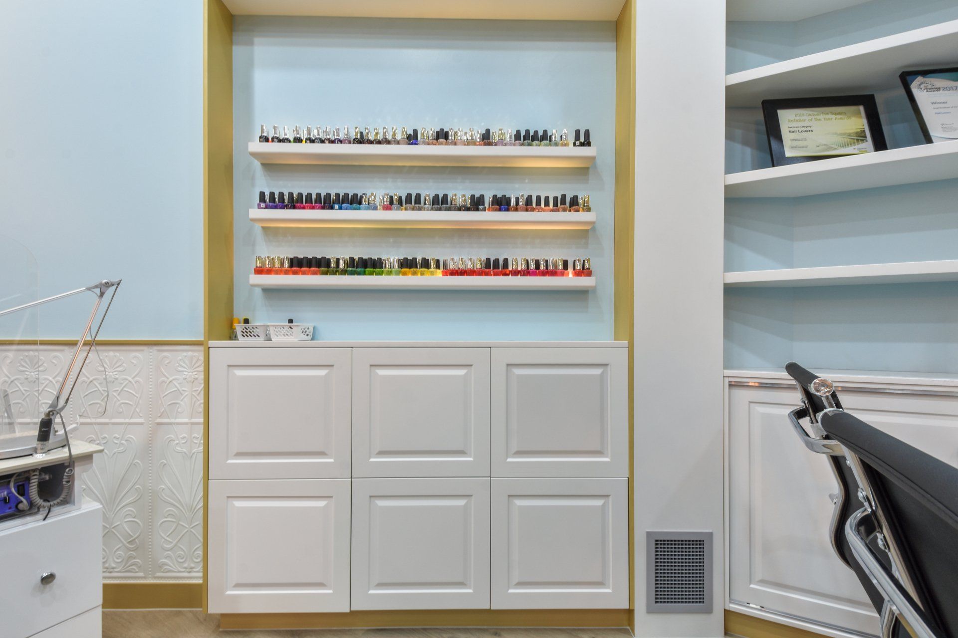 Nail salon interior with white cabinets, shelves of nail polish, light blue walls, and a work station.