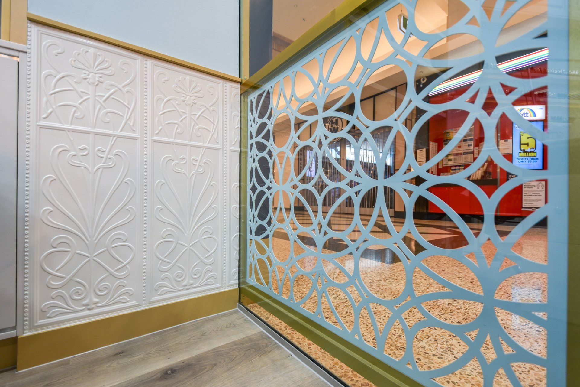 Ornate white wall panels and a decorative laser-cut screen, with a view into a brightly lit interior.