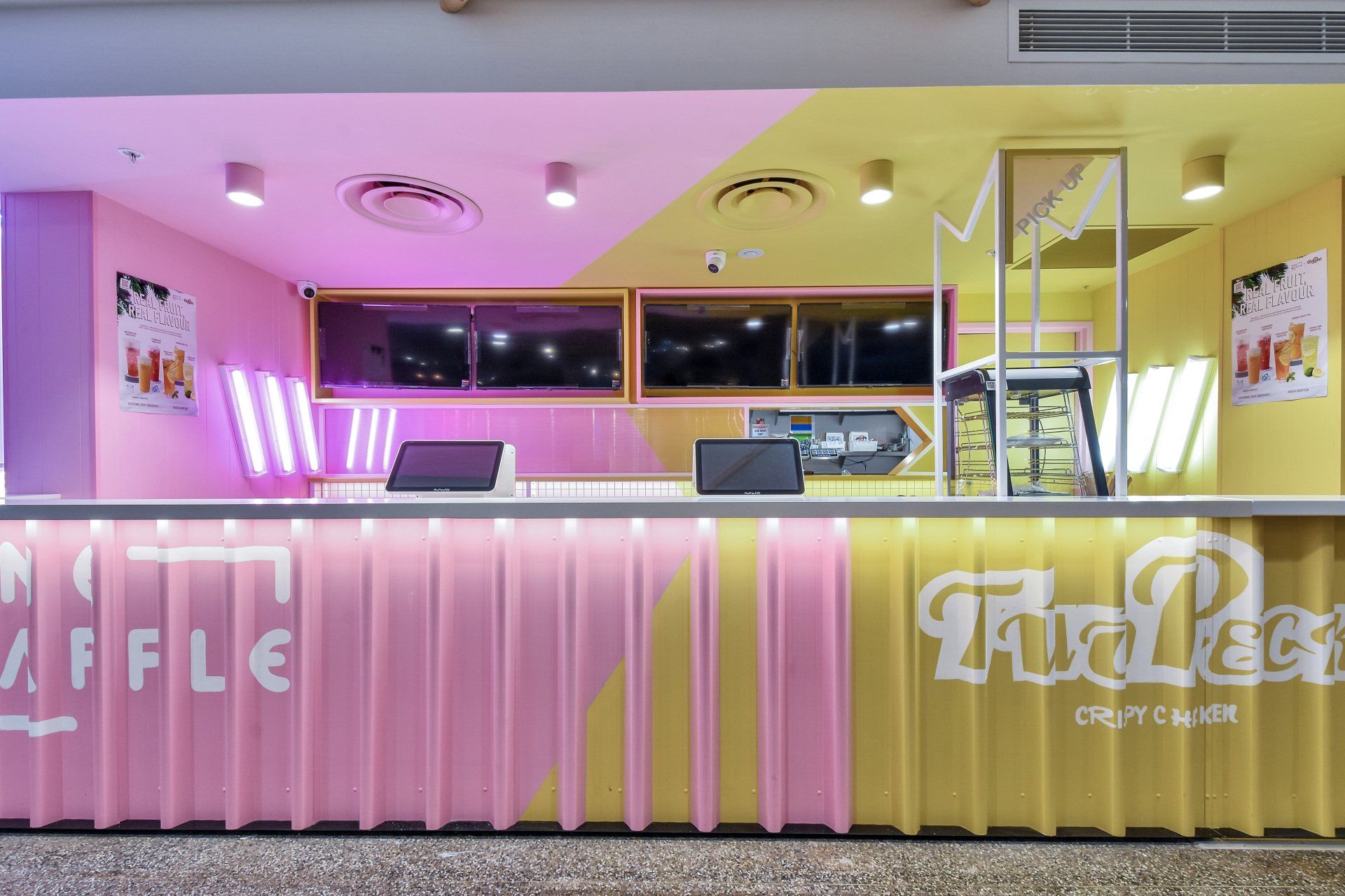 A brightly colored cafe counter with pink and yellow panels, serving drinks and waffles.