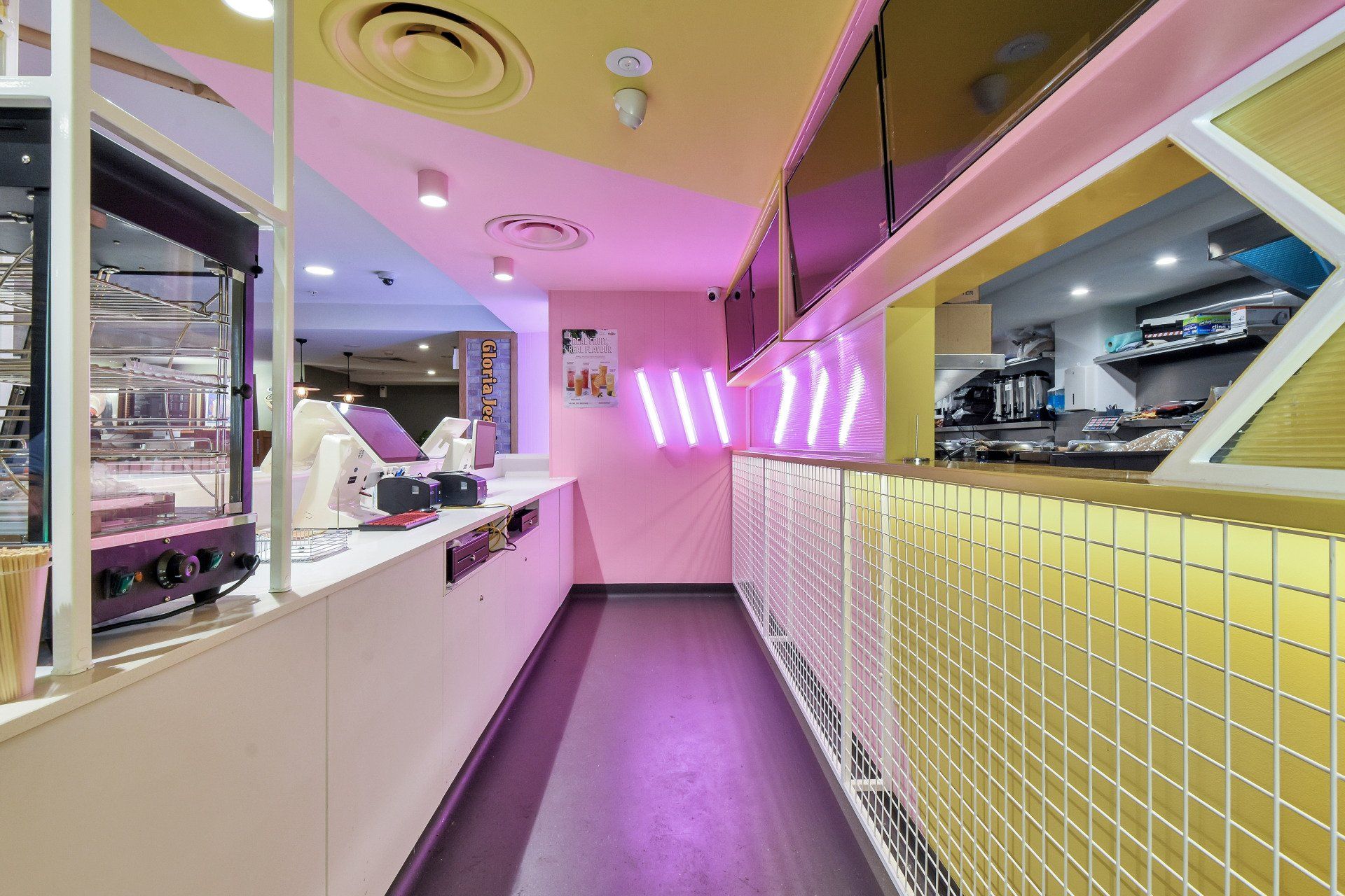 Interior of a colorful shop with a white counter and pink neon sign.