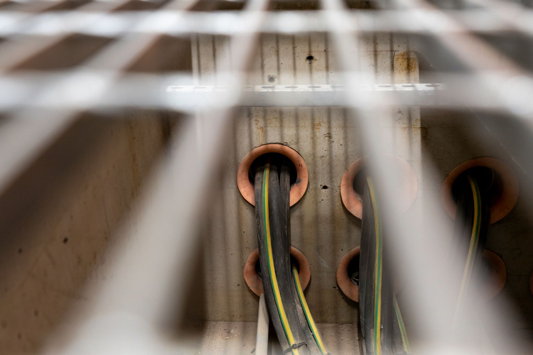 Metal grate covering a wooden box with electrical cables emerging through rubber grommets.