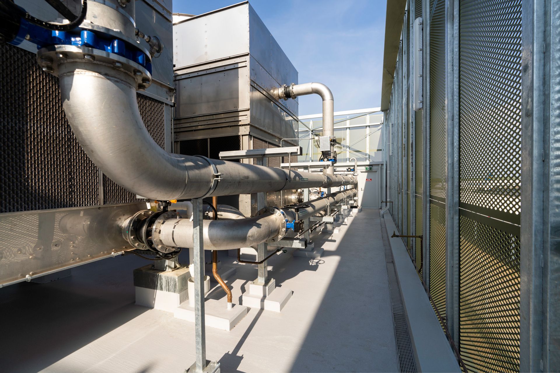 Metal pipes and industrial machinery on a rooftop platform next to a building with perforated metal siding.
