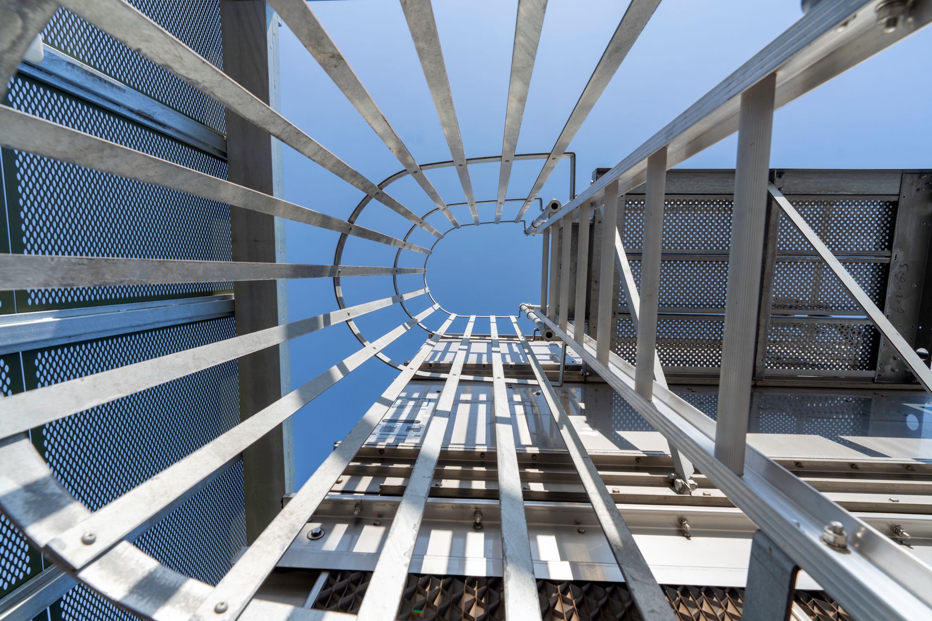 Low-angle view of a metal ladder leading to a circular opening against a blue sky.