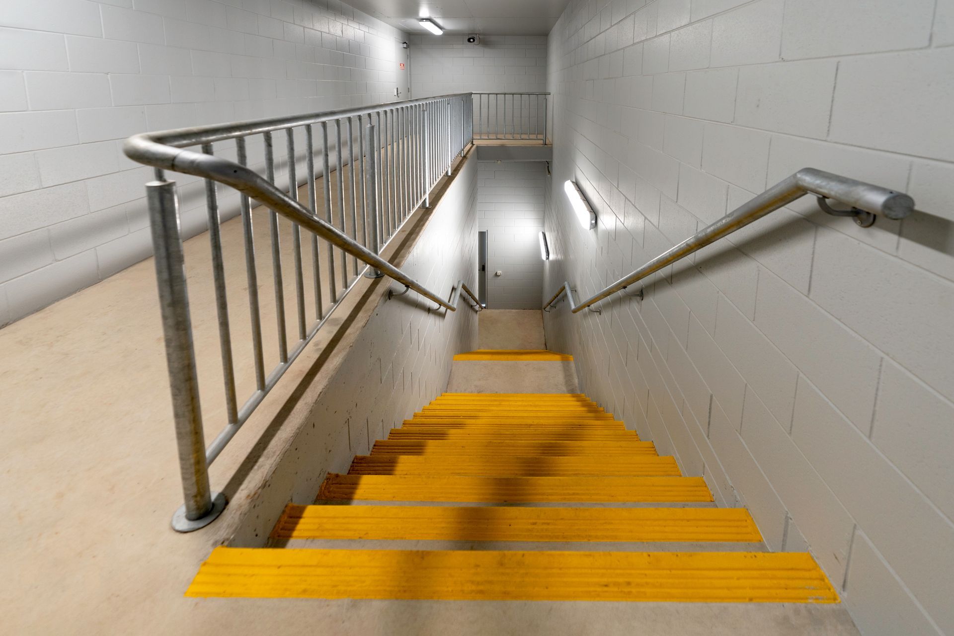 Staircase with yellow treads and metal railings descending into a gray-walled hallway.