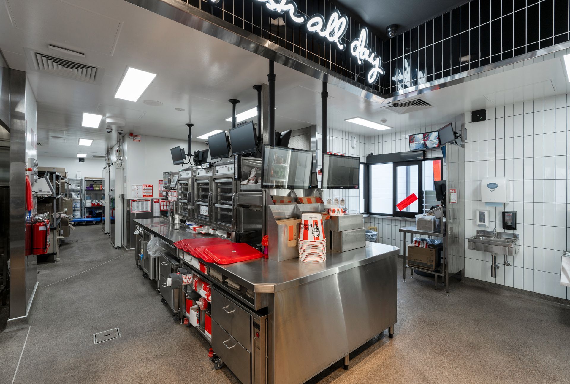 Restaurant kitchen interior: stainless steel counters, cooking equipment, food prep area, bright lights.