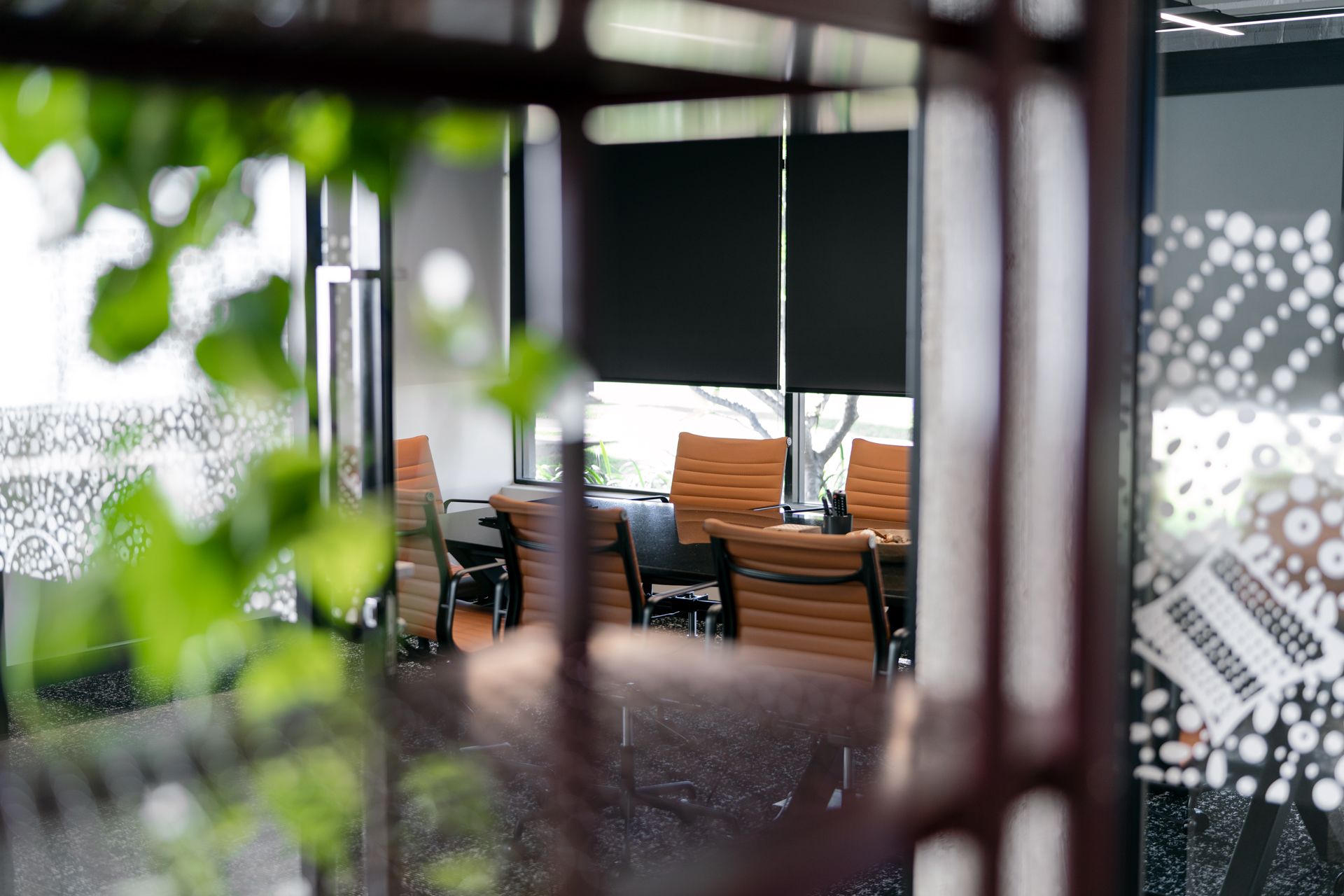 Conference room with brown leather chairs visible through a blurred, leafy foreground and patterned glass.