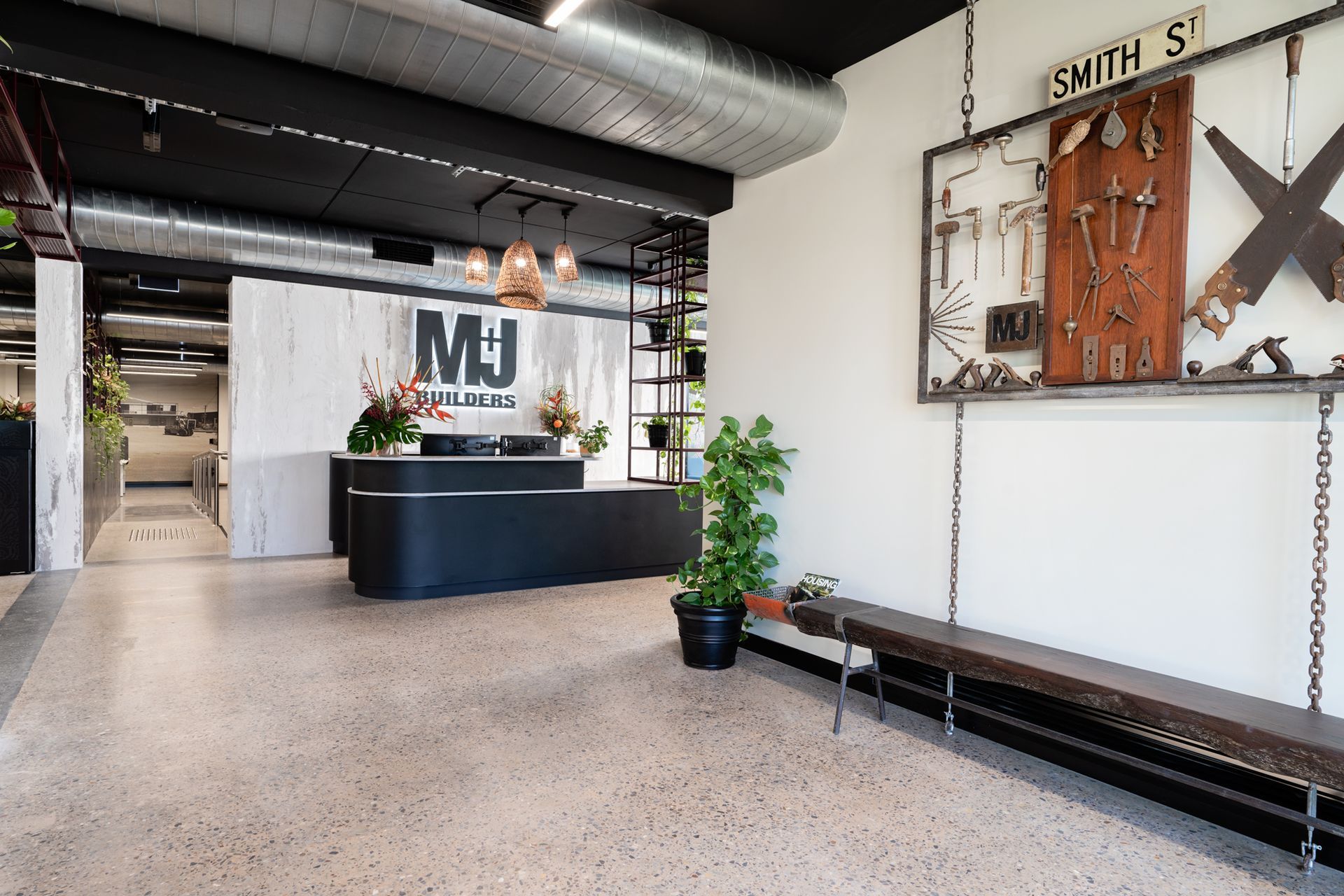 Modern office reception area with black desk, terrazzo floor, tool display, and hanging bench.