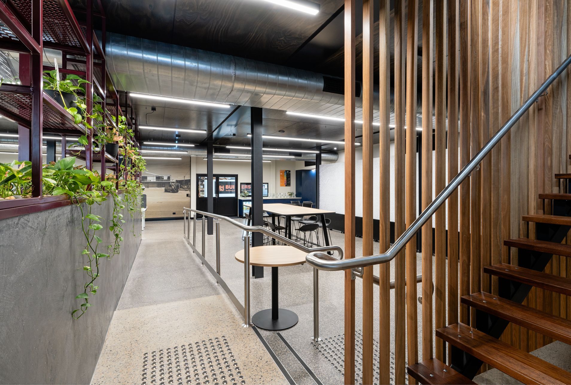 Stairwell with wooden slats, tables, and plants. Indoor space with metal railings and concrete walls.
