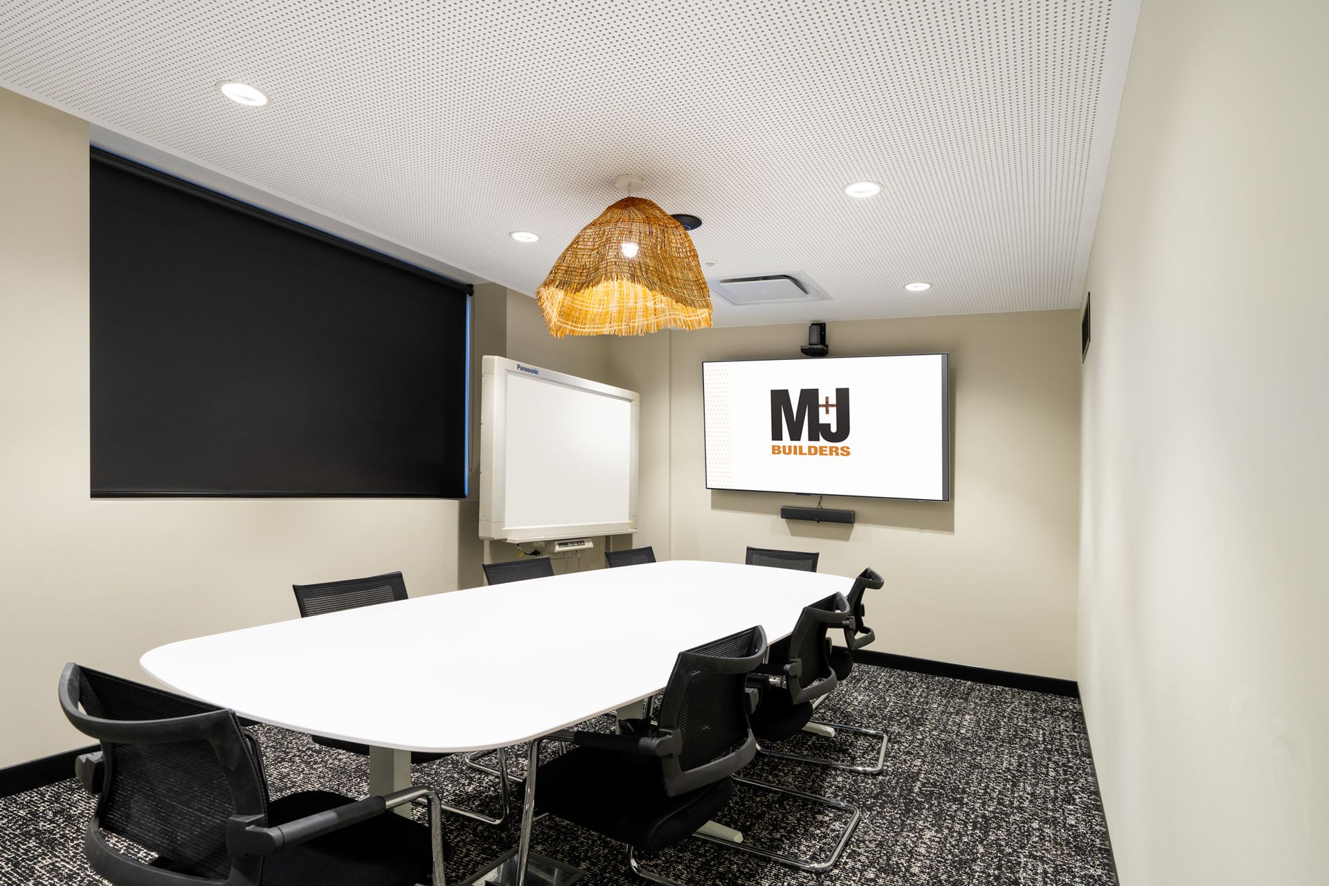 Conference room with a white table, chairs, whiteboard, screen displaying 