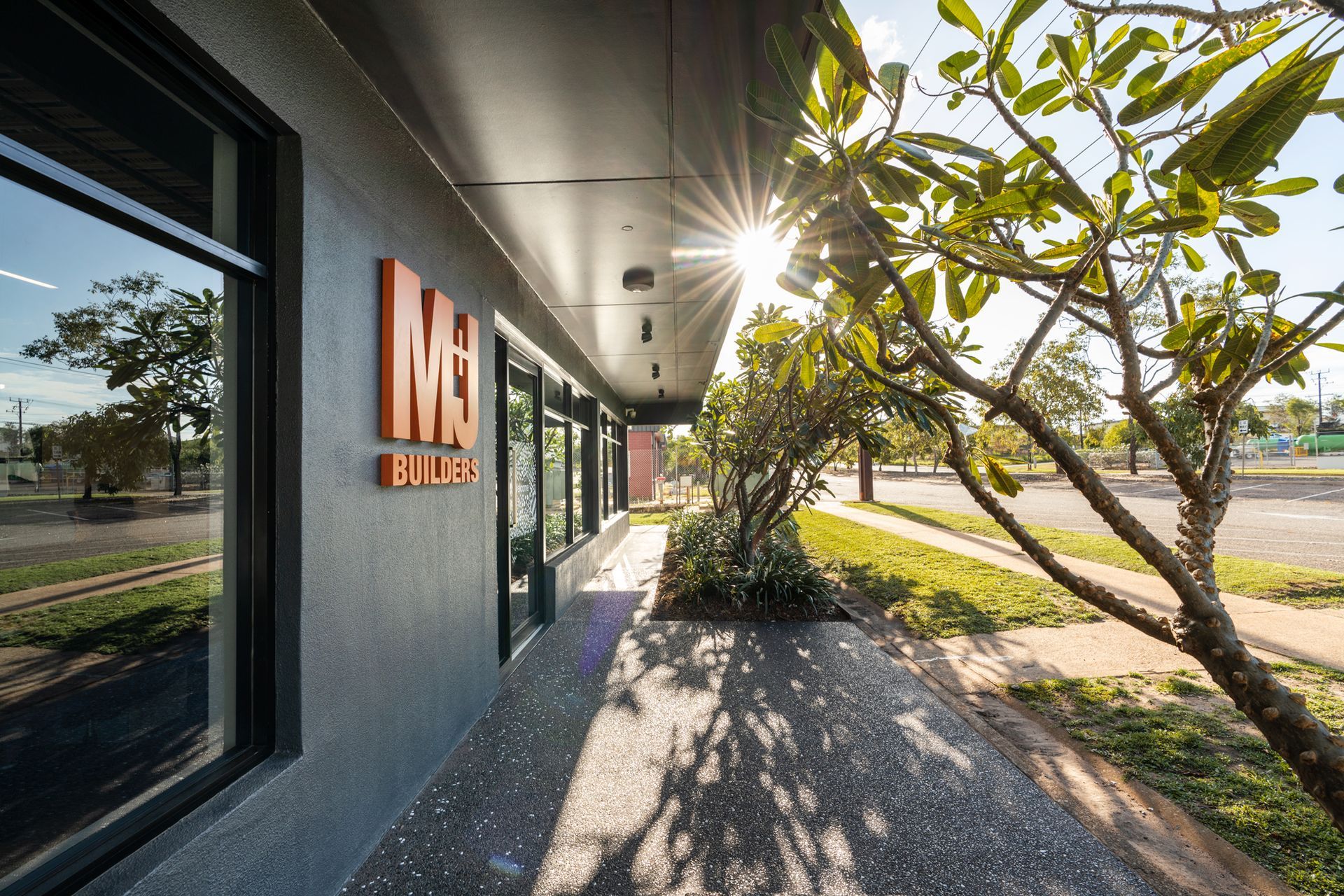 Exterior of M&B Builders building with orange logo and bright sunlight.