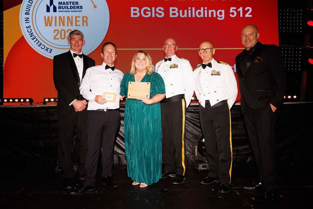 Group of people on a stage; winners with awards in front of a BGIS Building 512 backdrop.