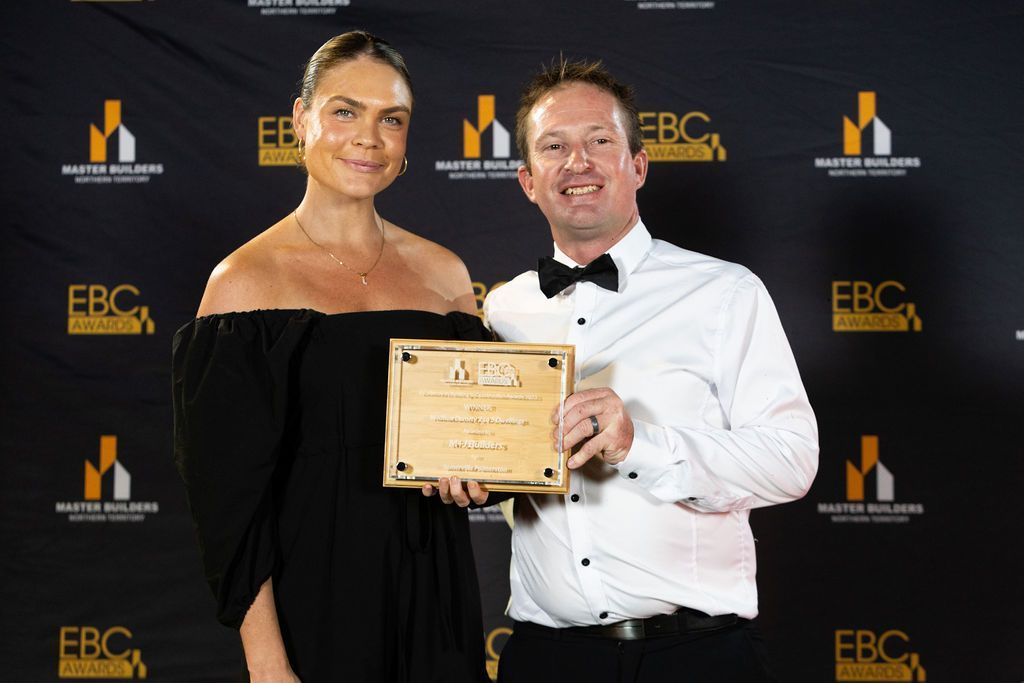 Woman in black dress and man in tuxedo holding award at event.