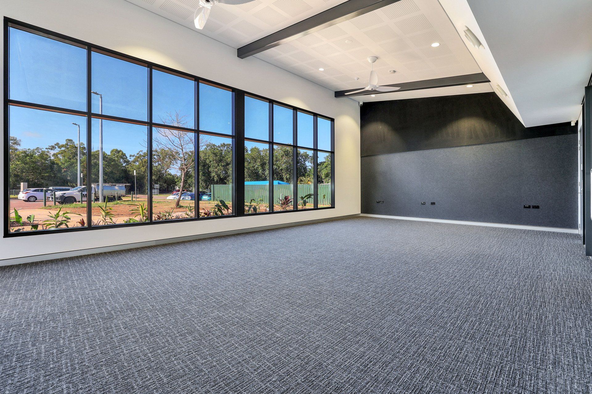 Empty room with large windows, grey carpet, black accent wall, and natural outdoor view.