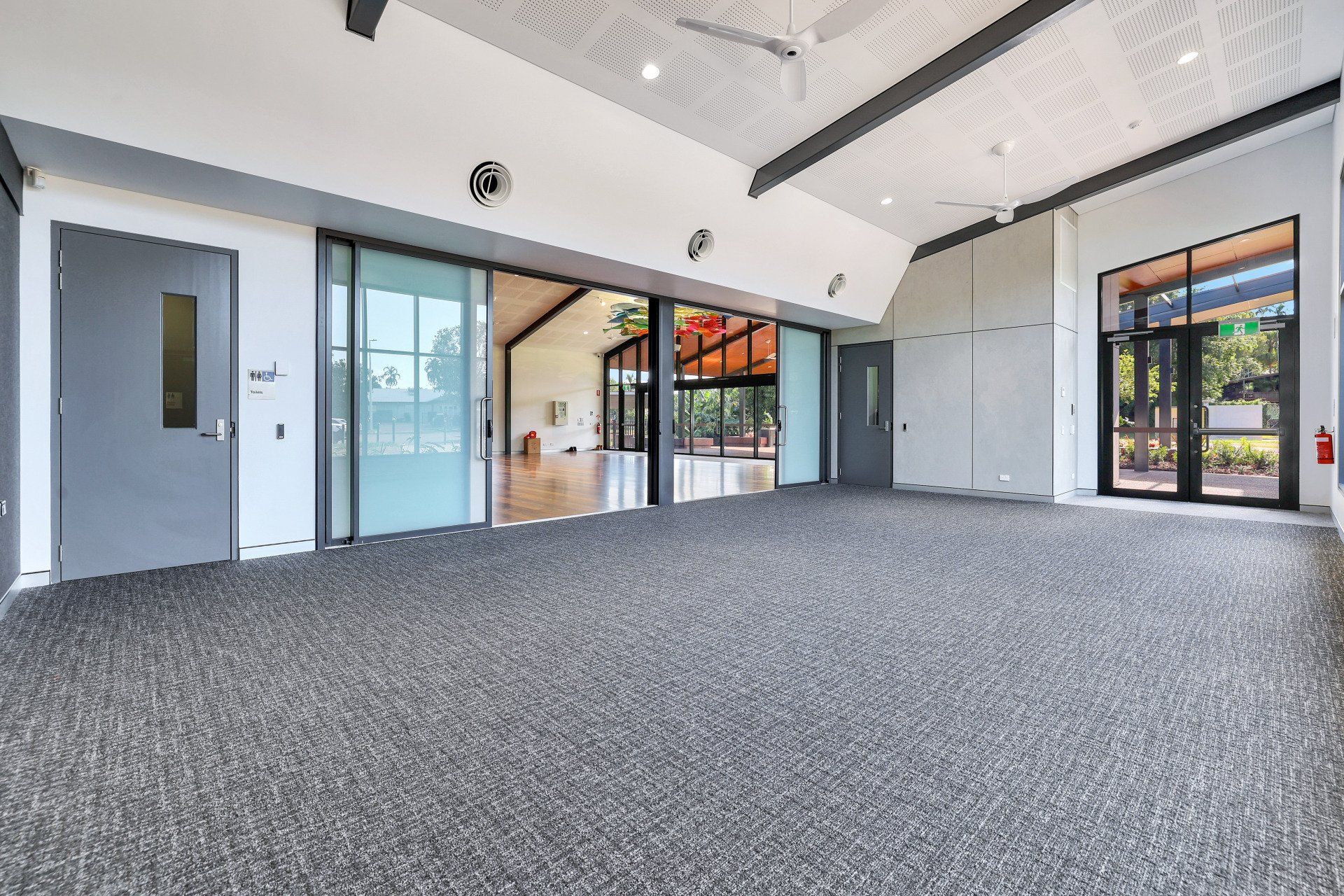 Empty, open-plan room with gray speckled carpet and large glass doors, leading to an outdoor space.