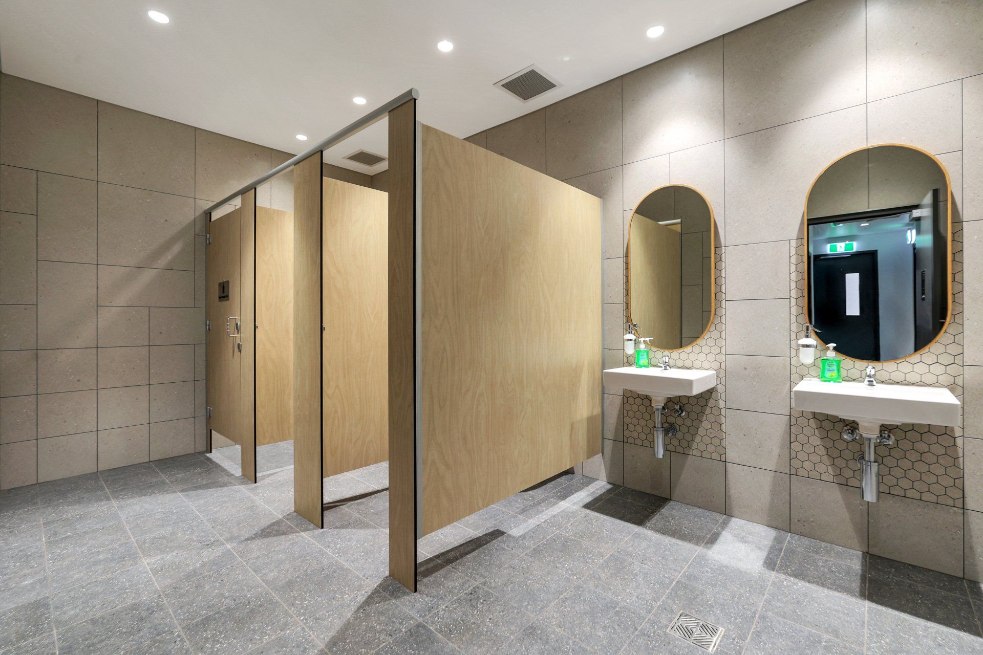 Public restroom with stalls, sinks, and mirrors. Neutral colors, modern design.