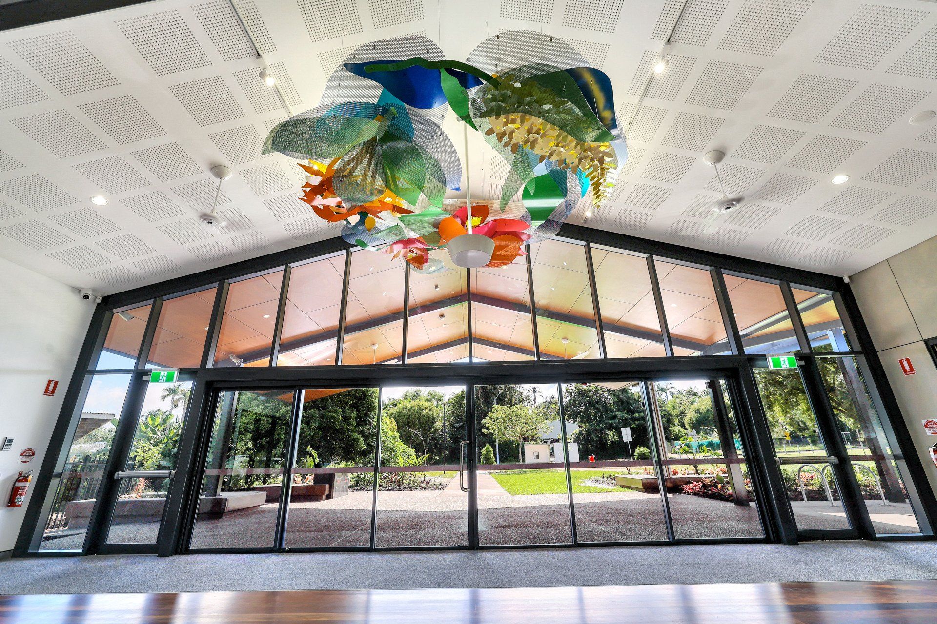 Entrance with glass doors, colorful artwork hanging from ceiling. Green yard visible through doors.