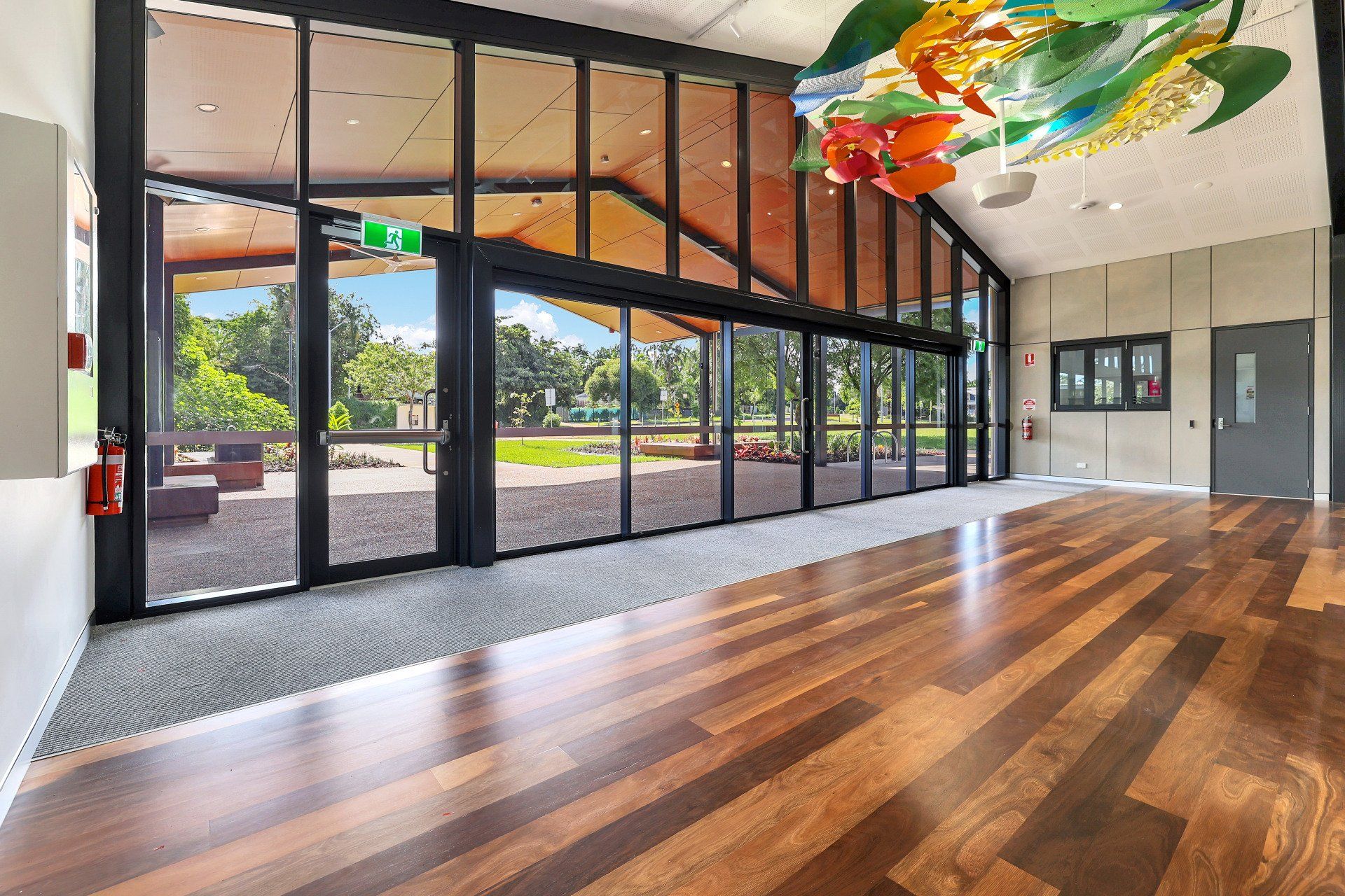 Spacious room with wooden floor and large glass doors opening to outdoor green space.