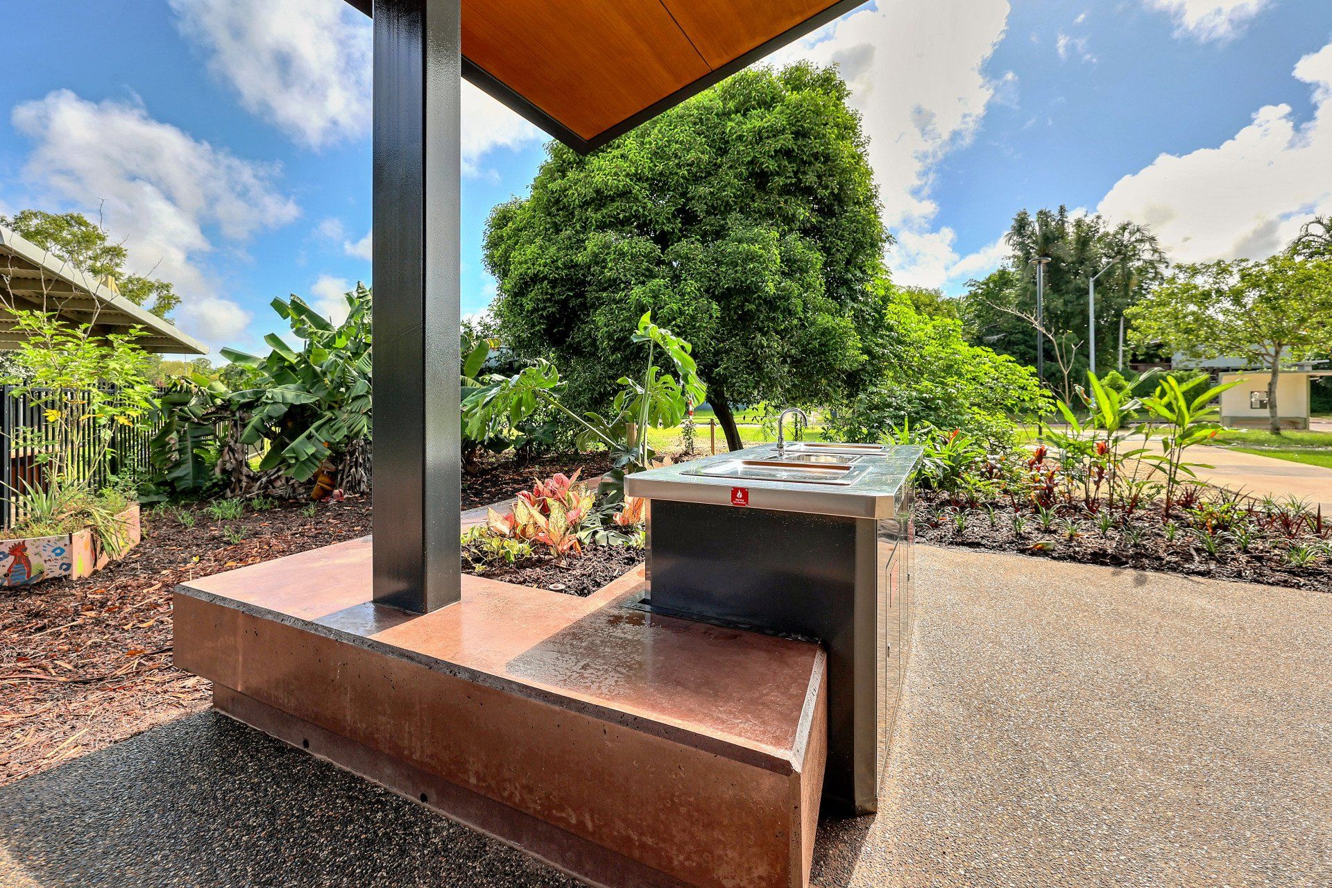 Barbecue in a park setting, with seating and foliage under a canopy.