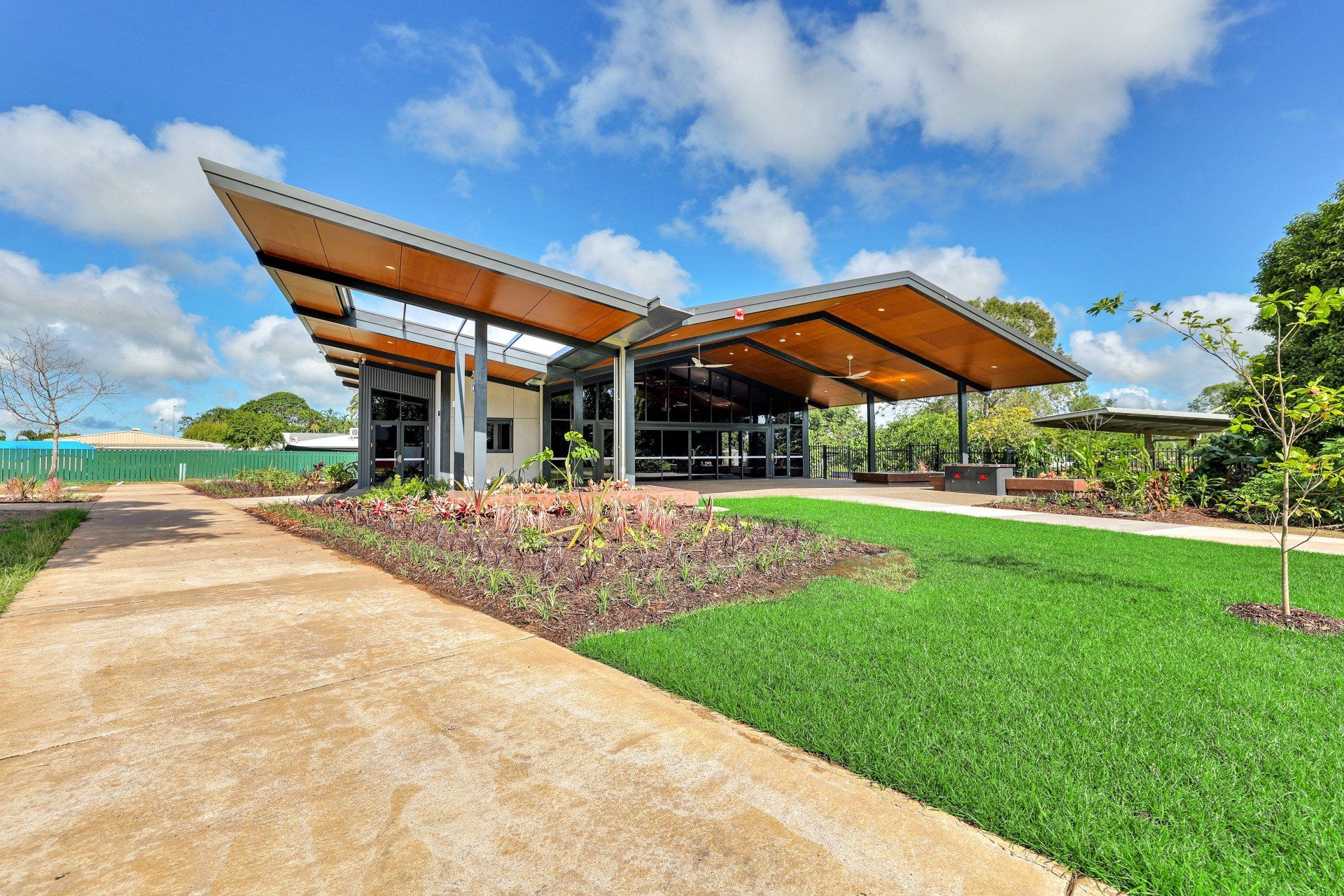 Modern building with angled roof, glass walls, and landscaped garden under a blue sky.