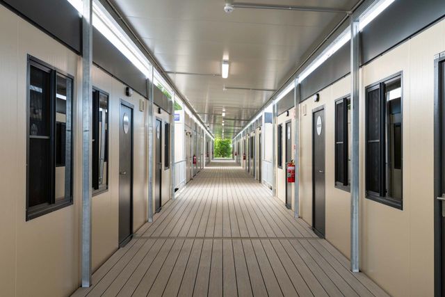 Corridor lined with modular units; tan walls, dark doors and windows, and metal supports.