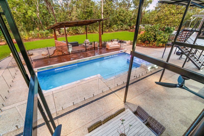 Outdoor swimming pool with lounge furniture, surrounded by greenery and a pergola.