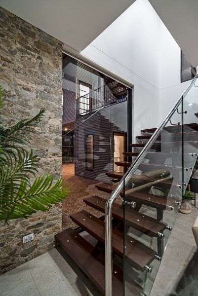 Interior view of a modern staircase with wooden steps, glass railing, and stone wall.