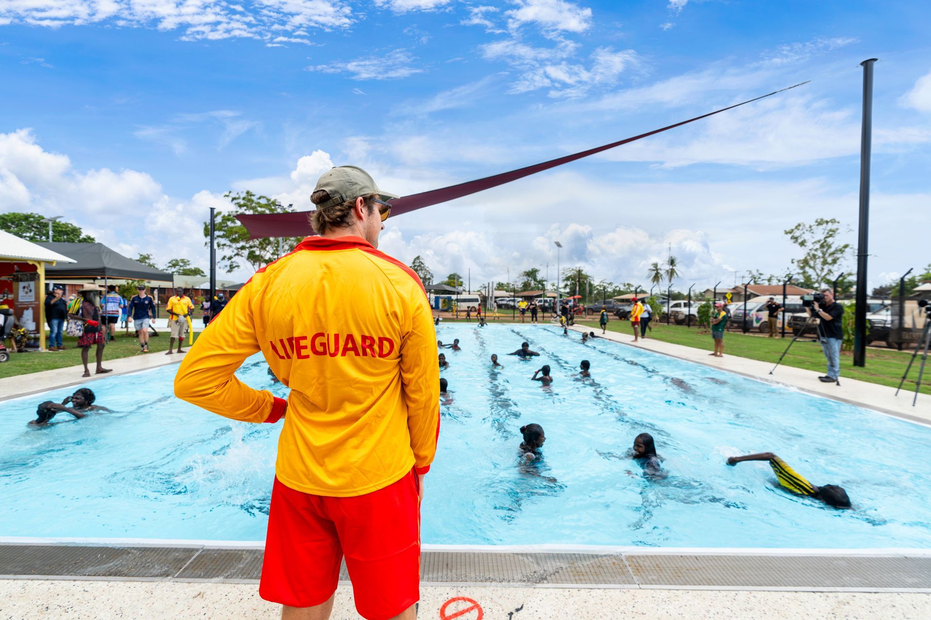 Lifeguard watches swimmers in a pool, under a blue sky.