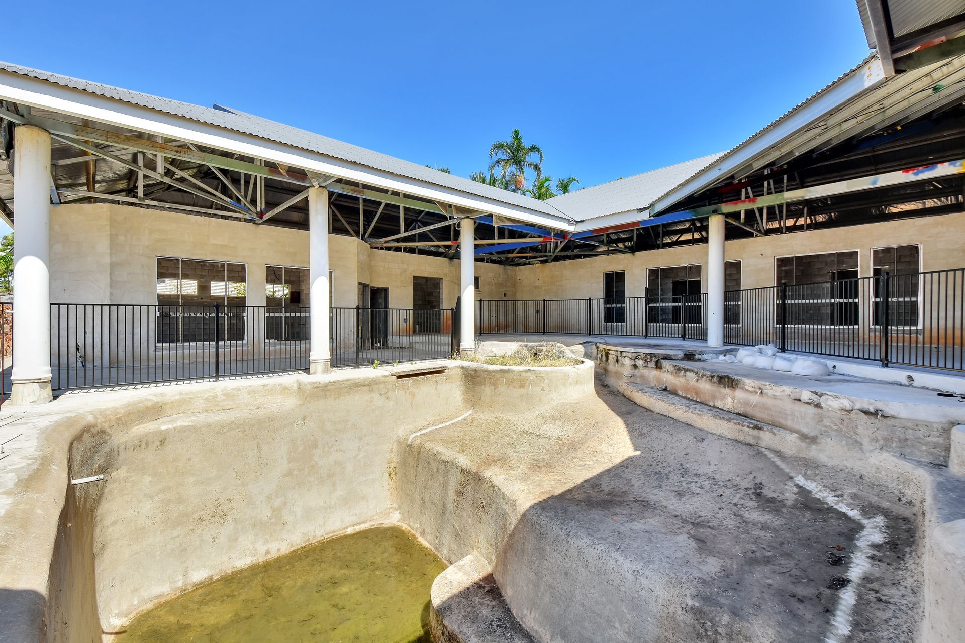 A concrete structure with open pens under a covered roof; bright blue sky.