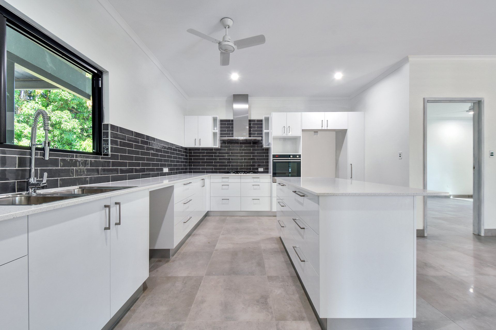 Modern white kitchen with black tile backsplash and an island, window with trees outside.
